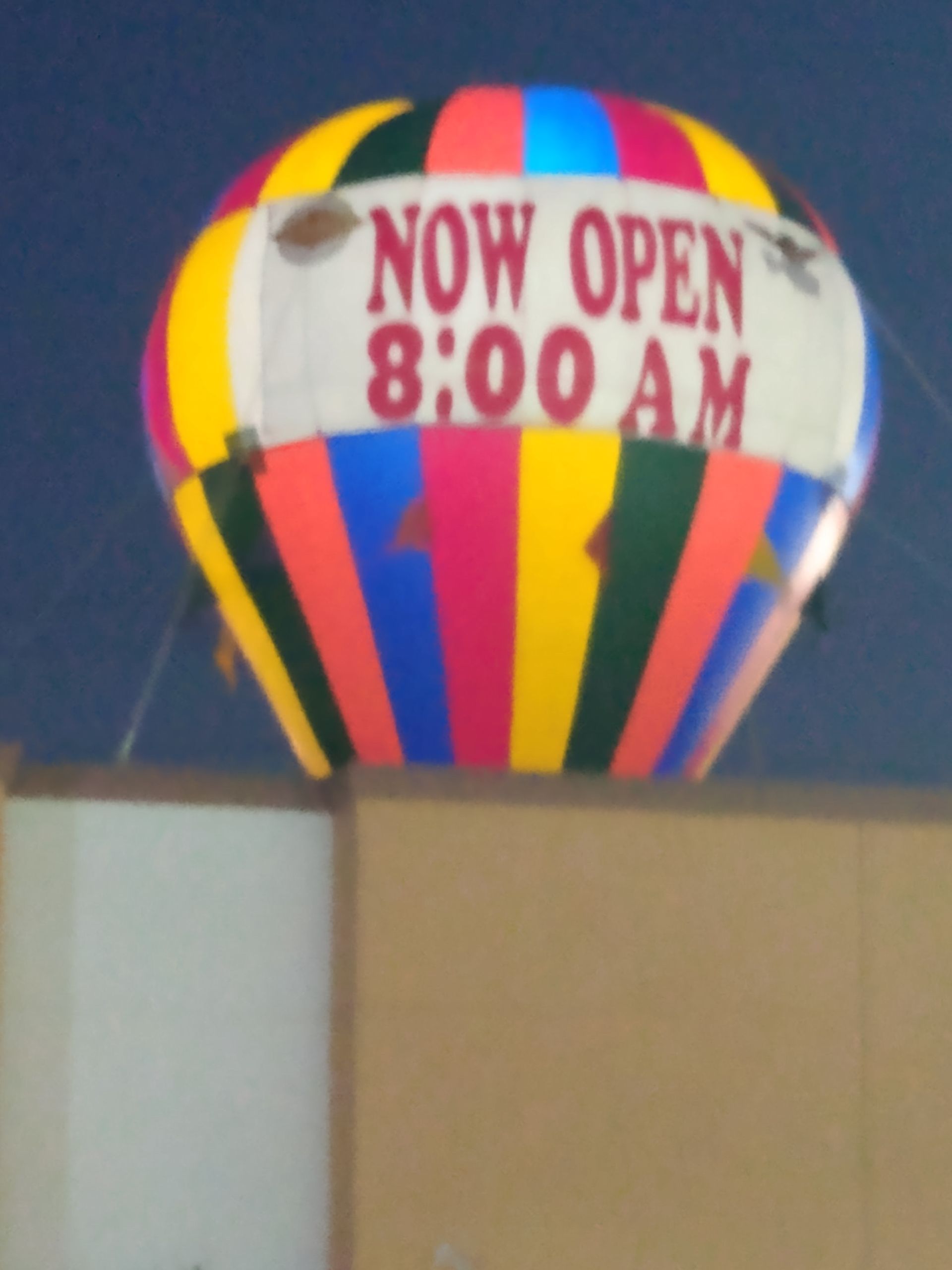 Colorful hot air balloon sign reading “NOW OPEN 8:00 AM” above a building