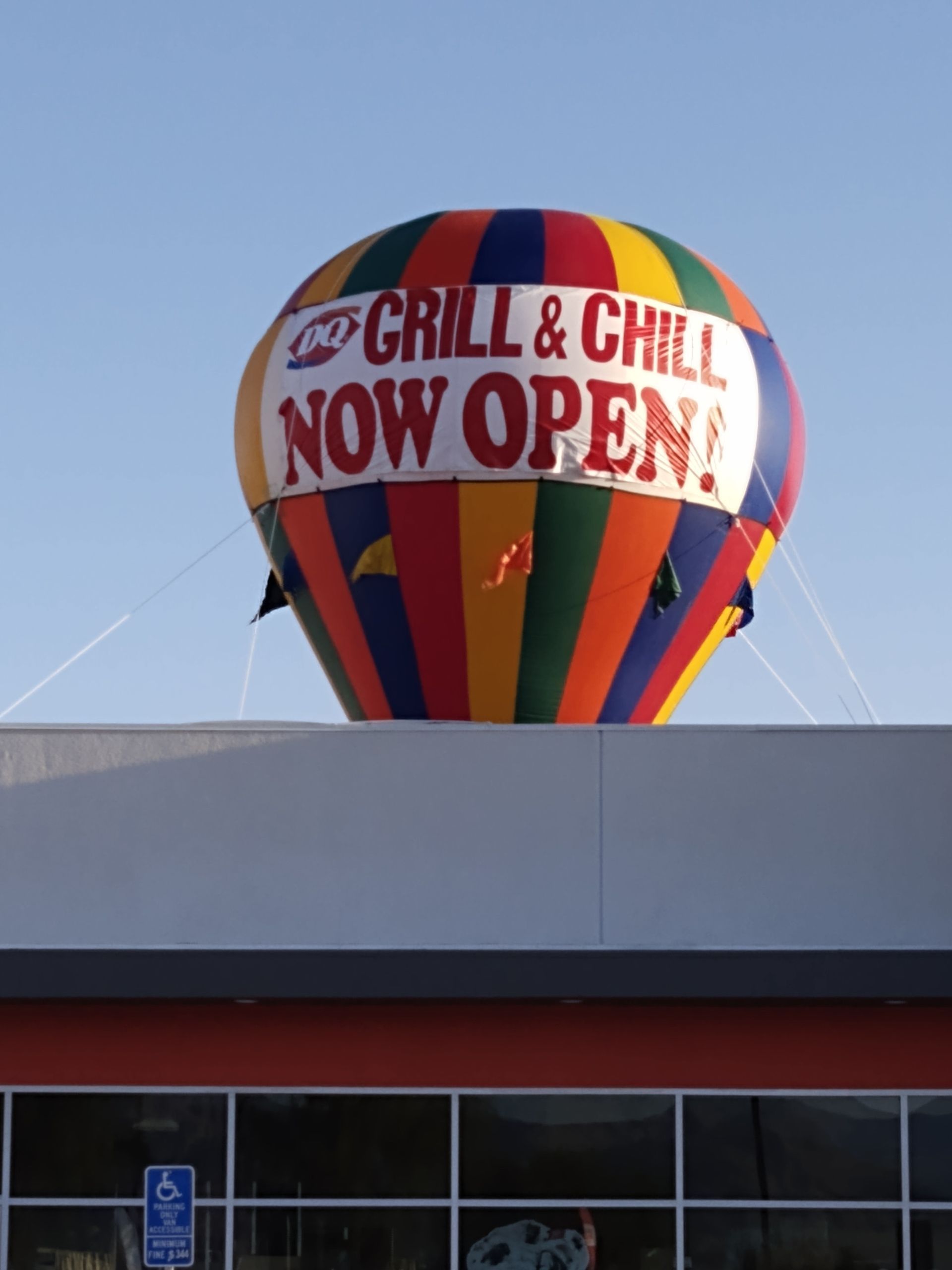 Colorful “Grill & Chill Now Open” hot air balloon above a building rooftop