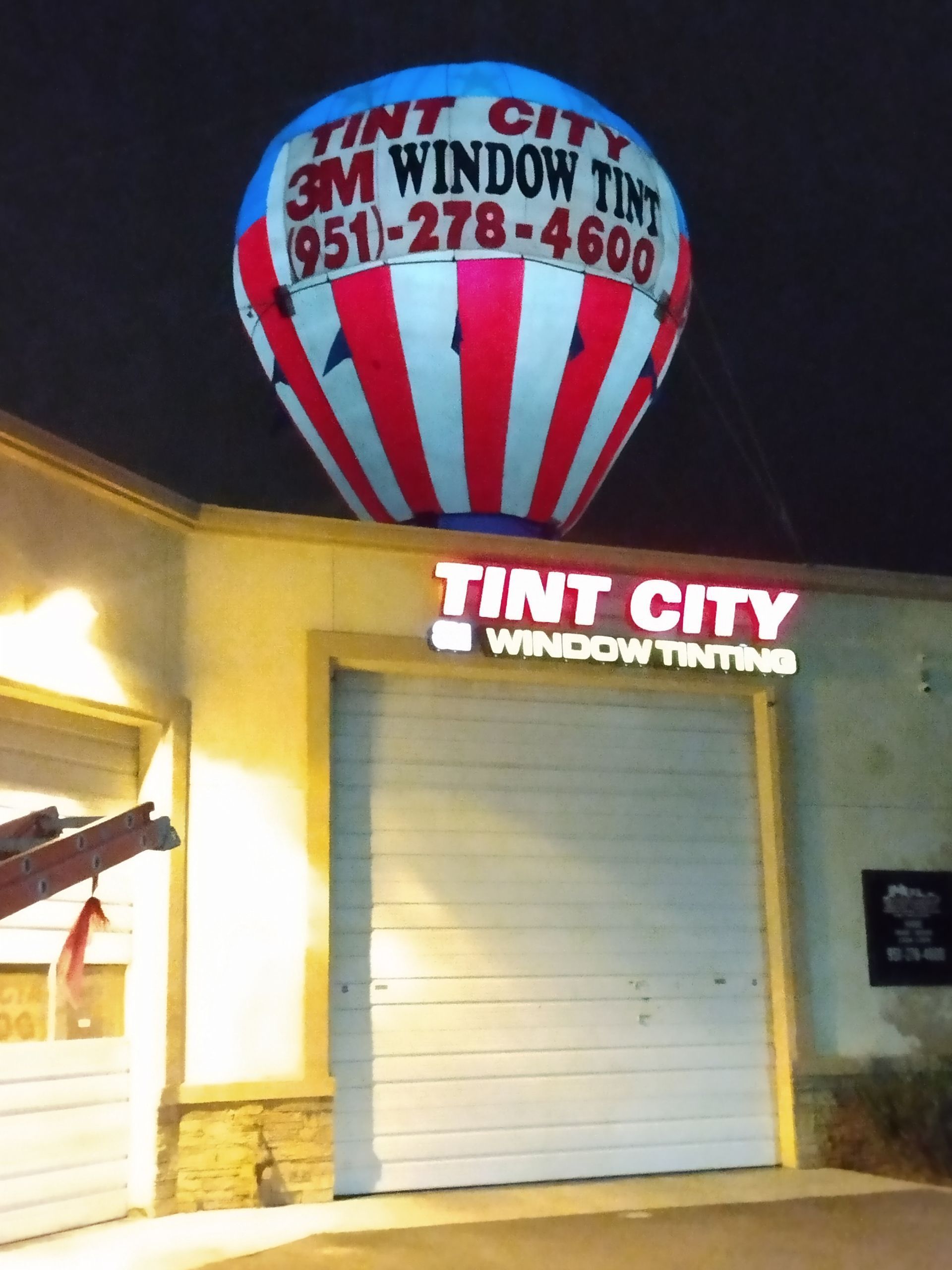 Tint City Window Tinting storefront at night with red, white, and blue sign and balloon logo