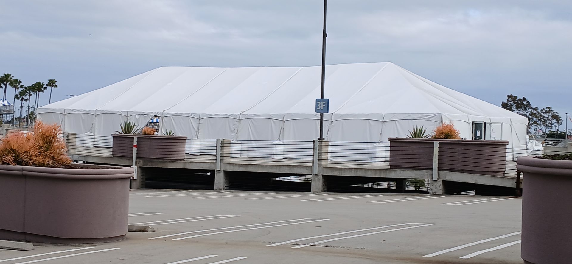 Large white event tent behind a wooden fence in a paved outdoor area