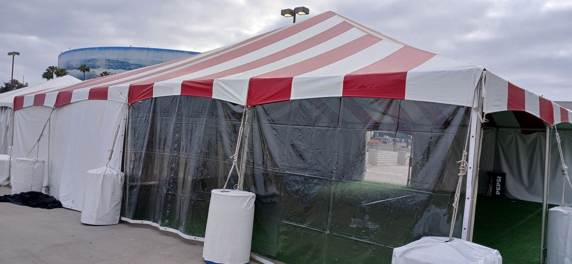 Red-and-white striped event tent with clear side panels and white barriers outdoors