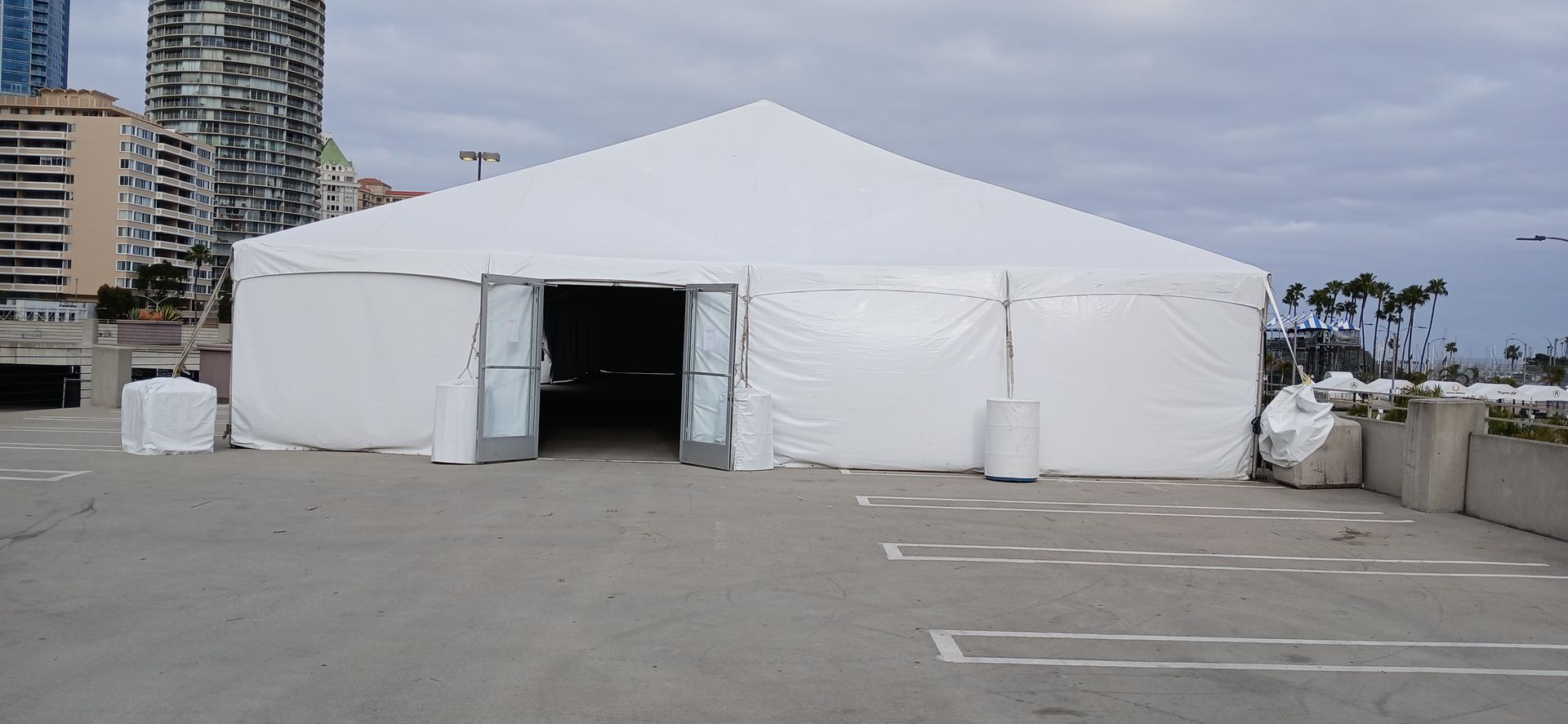 Large white event tent set up in an empty parking lot with city buildings in the background