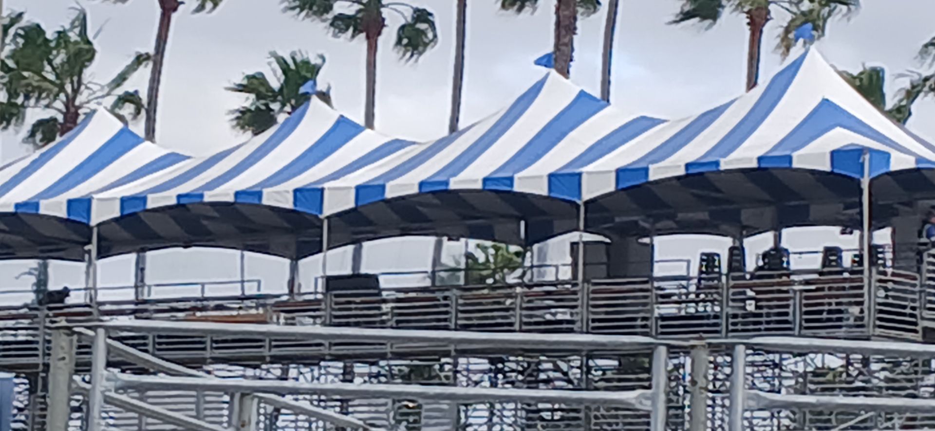 Blue-and-white striped event tents in a parking lot with palm trees in the background