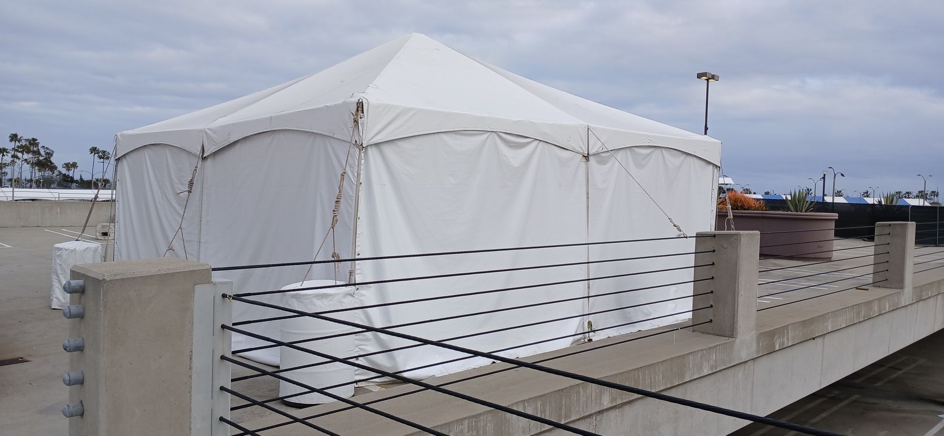White tent on a rooftop terrace with concrete planters and a view of the city at dusk