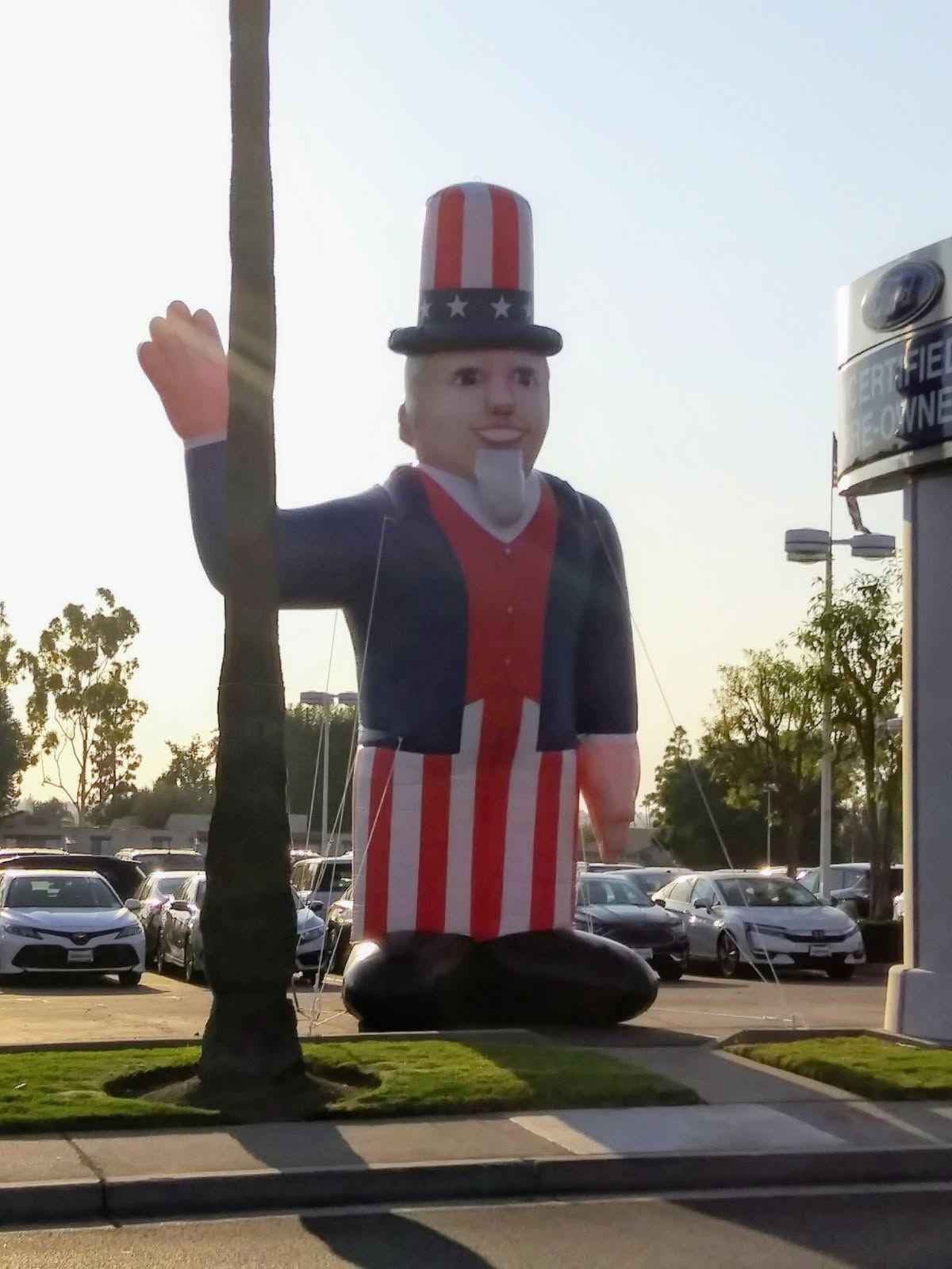 Large Uncle Sam inflatable standing on a sidewalk near parked cars and palm trees under a bright sky