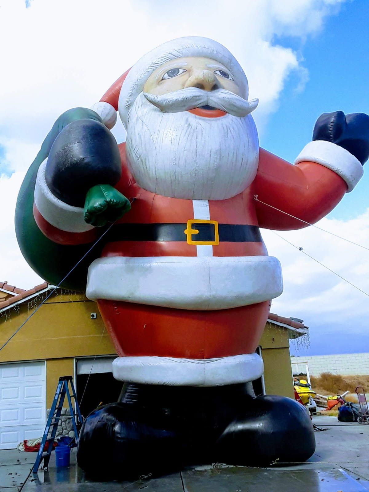 Giant inflatable Santa Claus waving outside a building, wearing a red suit, black boots, and white beard