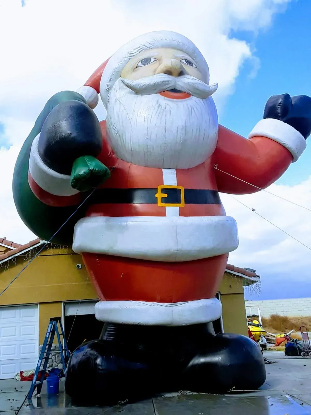 Huge inflatable Santa in red suit outside a building, waving with one hand and holding a sack over his shoulder