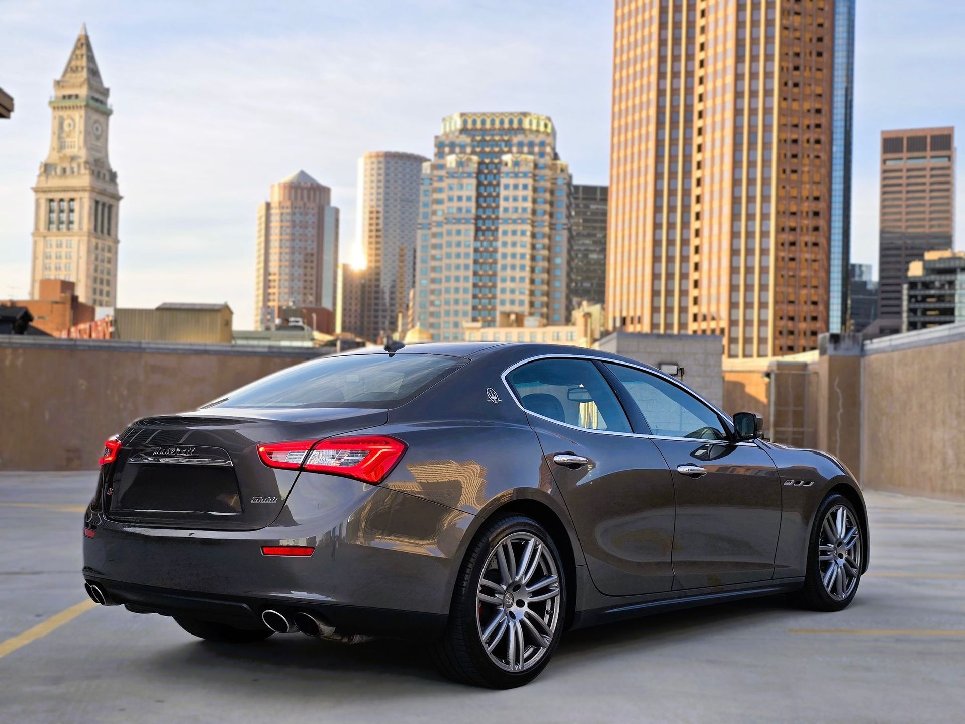 Dark gray sedan parked on a rooftop with a city skyline in the background