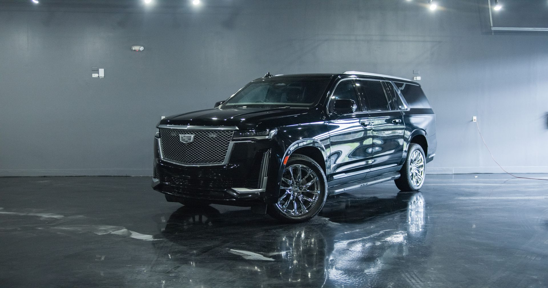 Black Cadillac Escalade SUV parked indoors with lights and reflective floor.