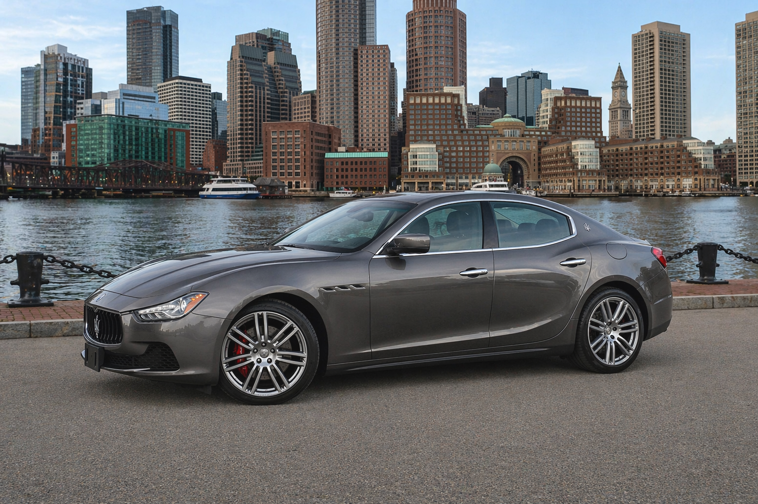 Gray sports sedan parked by a waterfront with a city skyline in the background