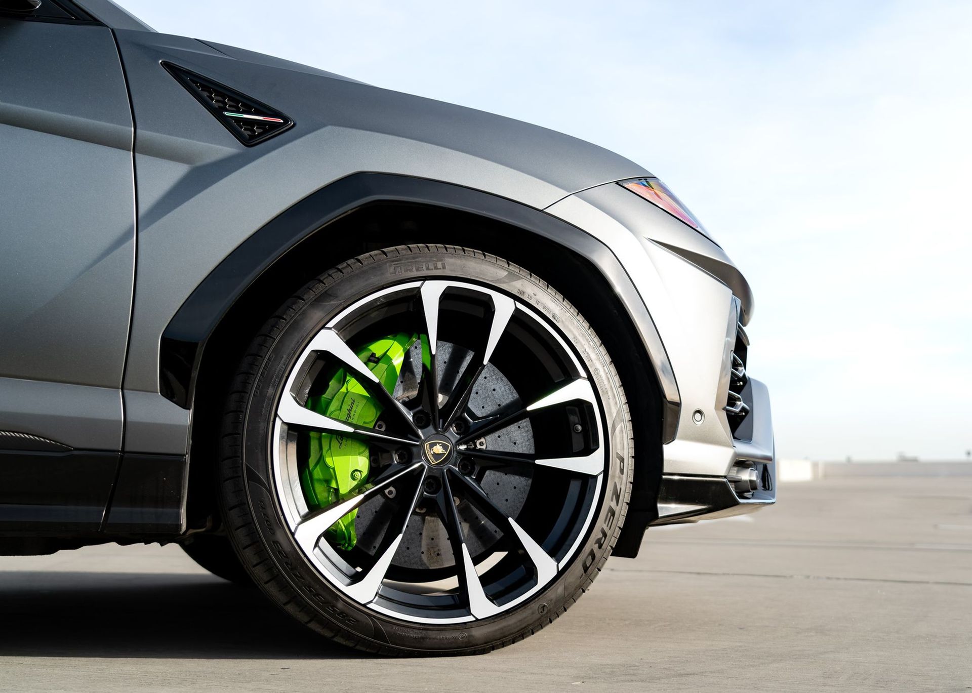 Close-up of a gray sports car’s front wheel with black rims and bright green brake calipers on a road.