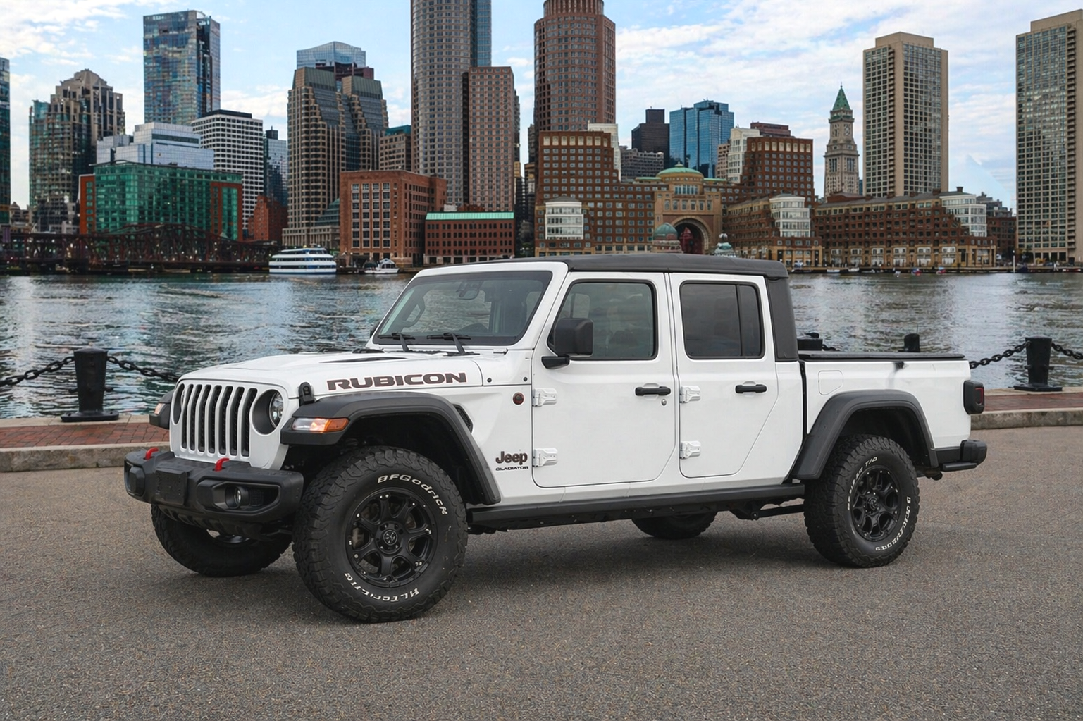 White Jeep Gladiator parked by the water with a city skyline in the background