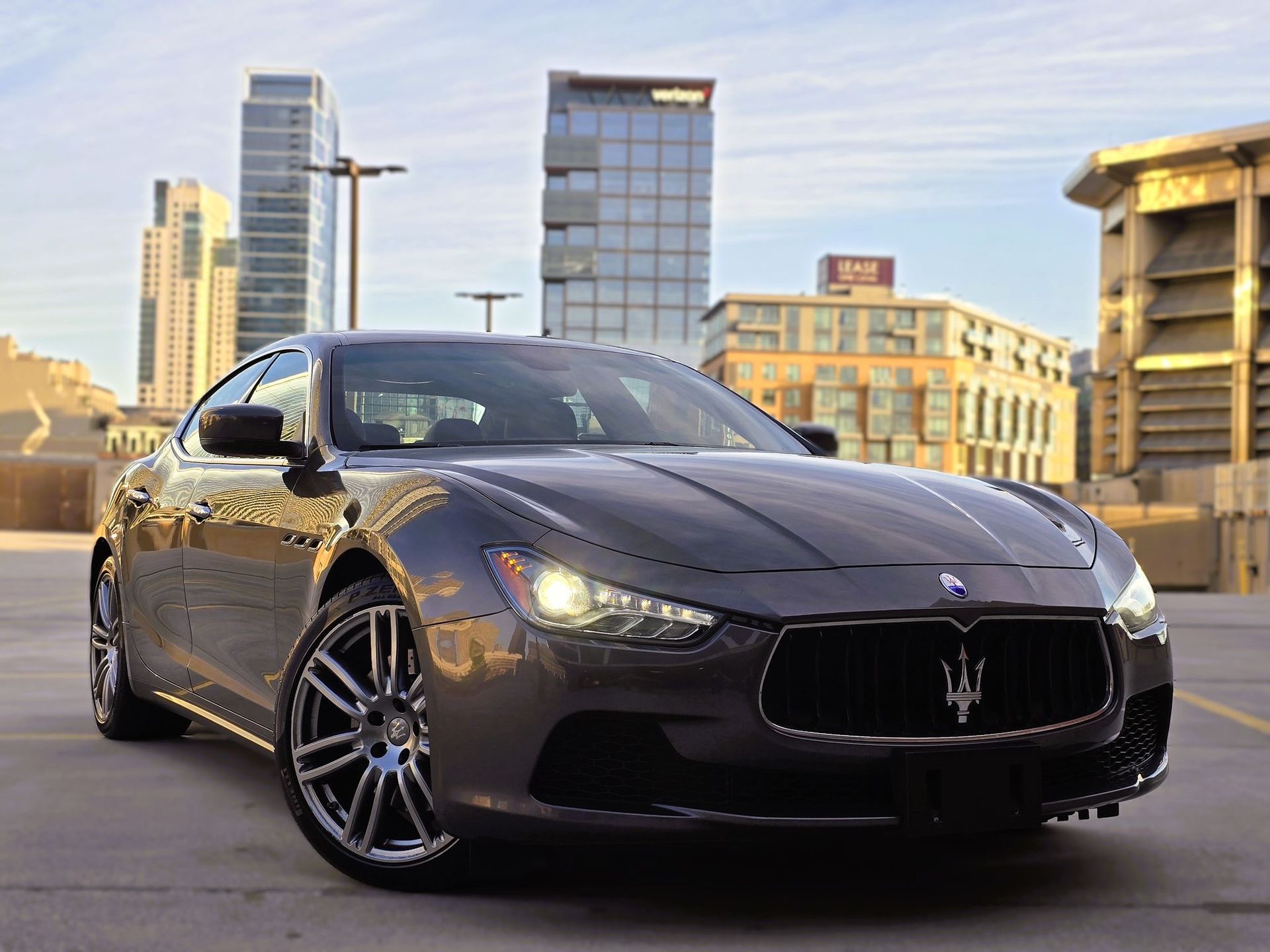 Dark gray Maserati sedan parked on a city street with downtown buildings in the background