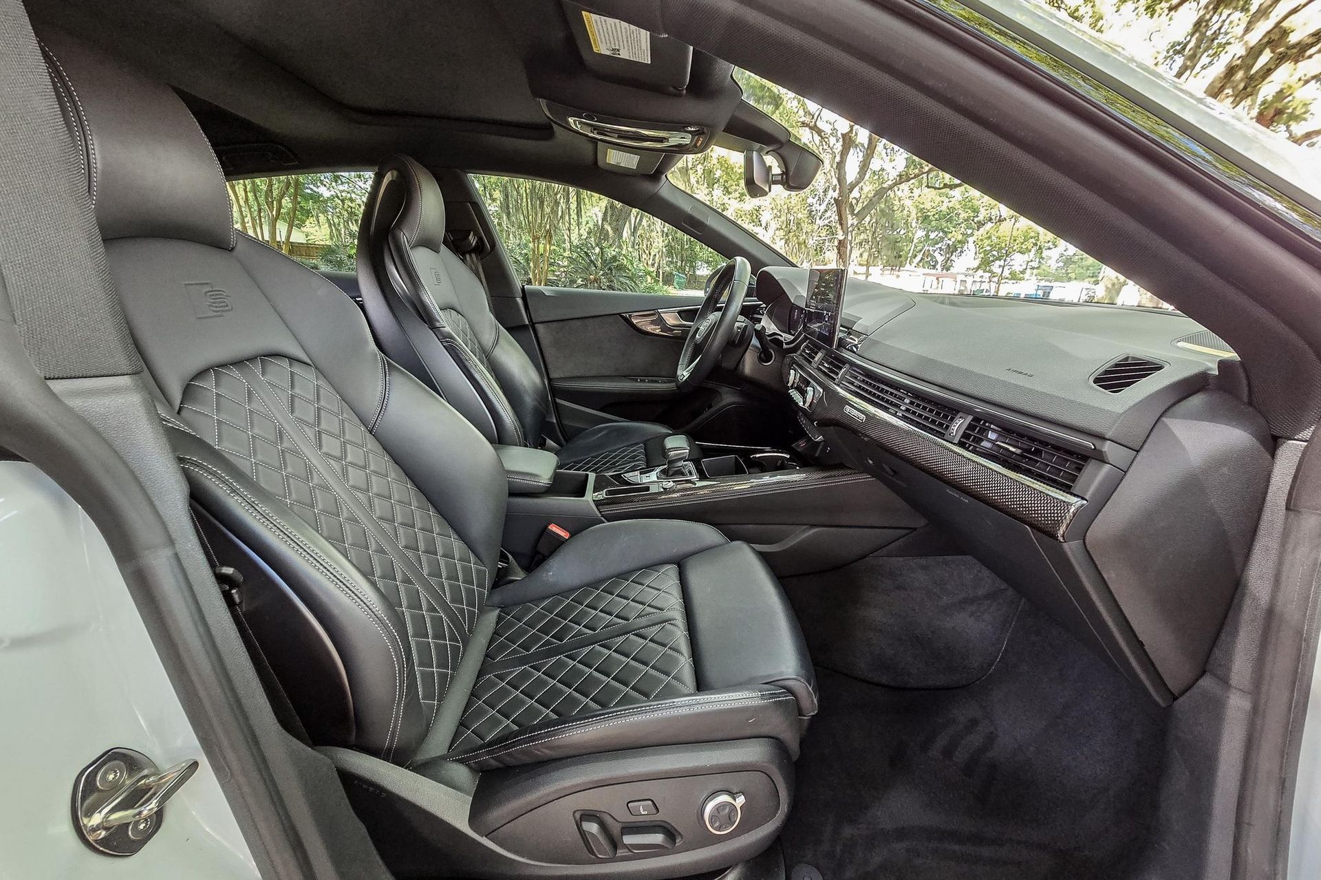 Car interior with black leather seats and patterned upholstery, viewed from the open passenger side.