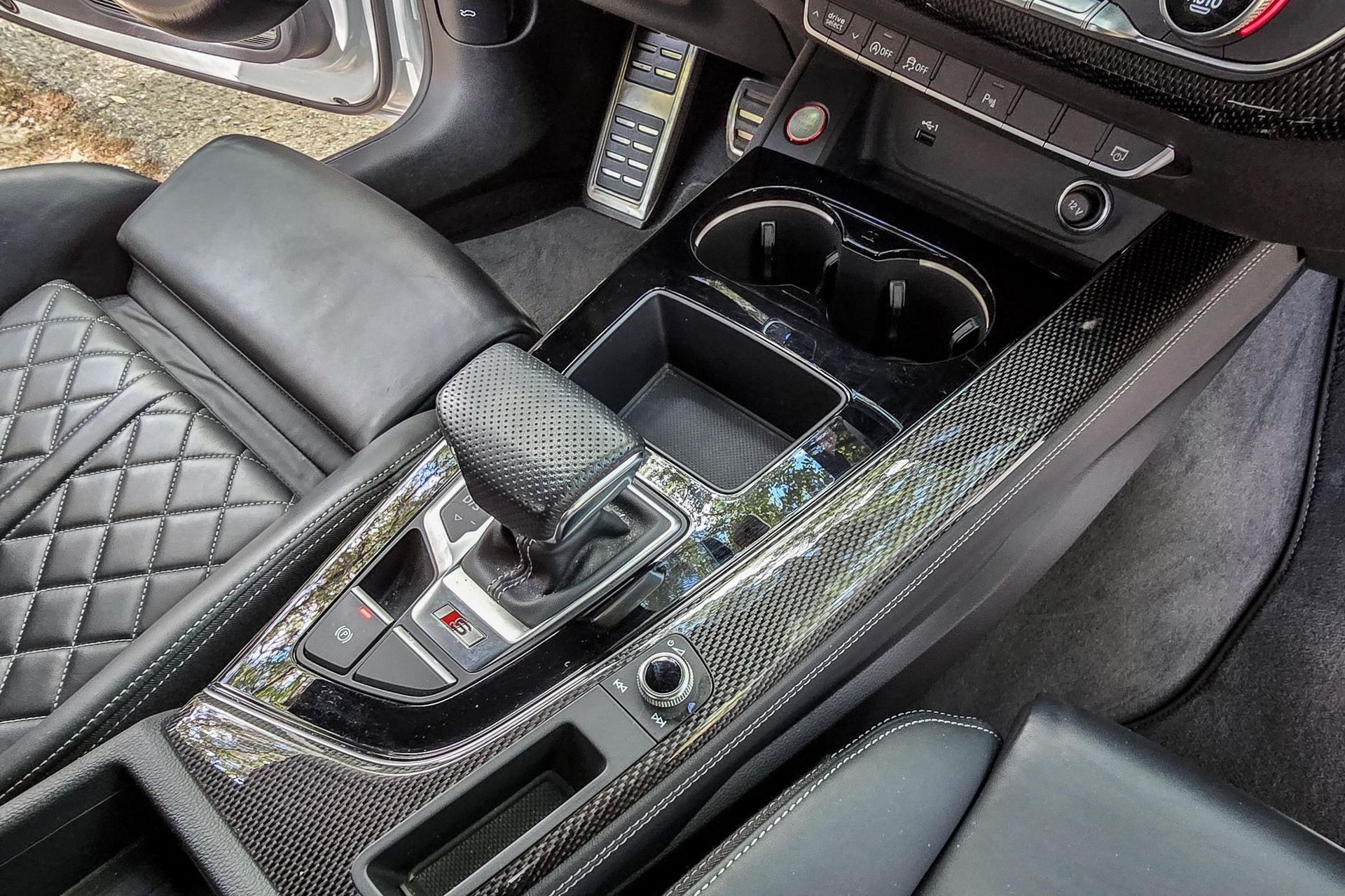 Luxury car interior with diamond-quilted black seats and a black center console covered in shattered glass.