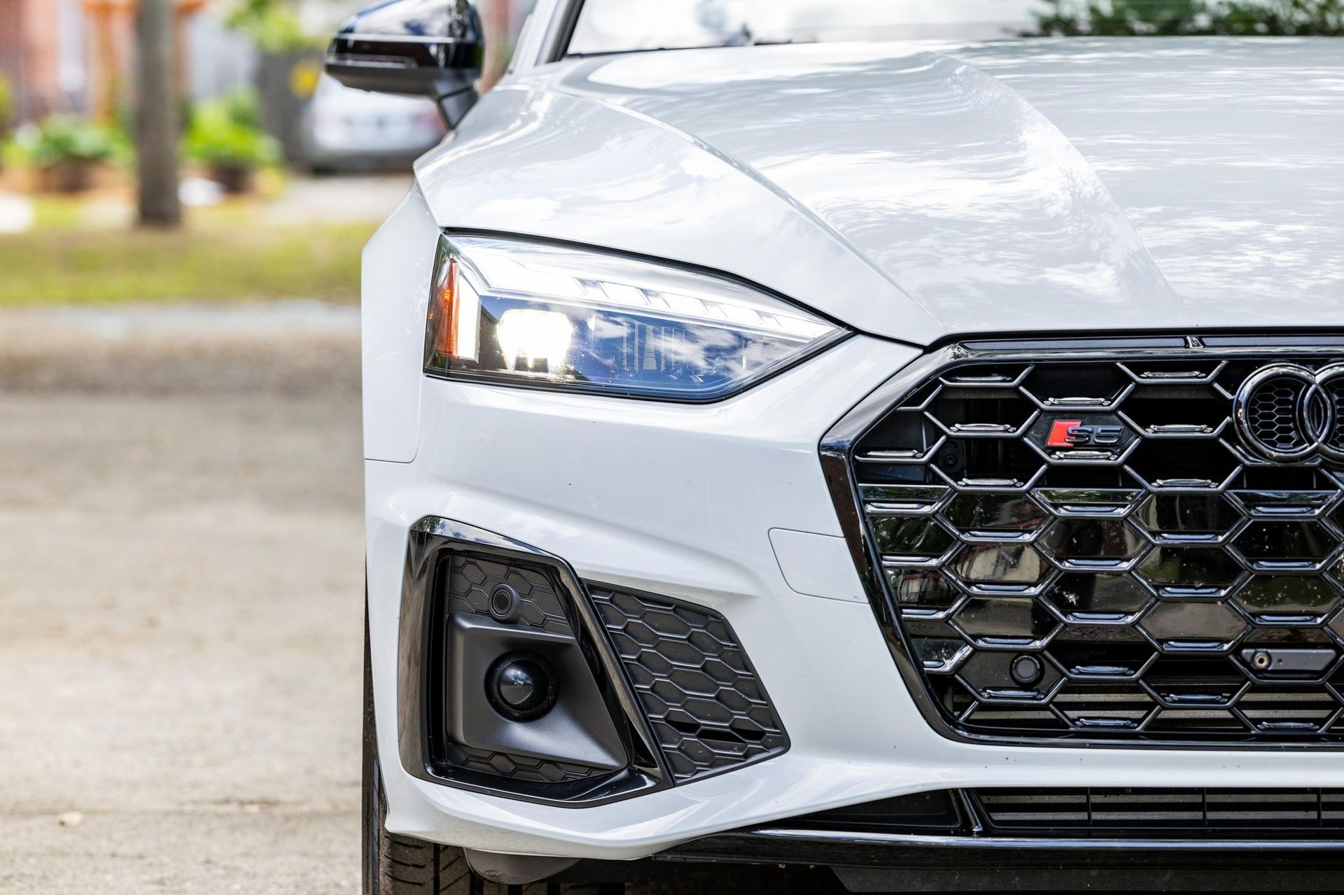 Front-left view of a white Audi car’s headlight and grille in a driveway