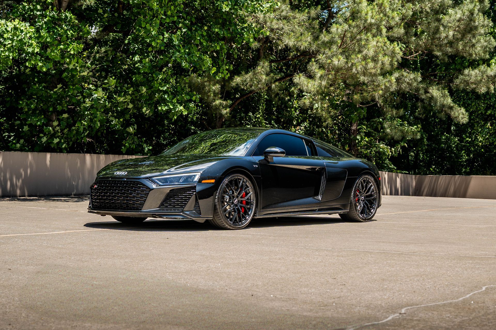 Black Audi R8 sports car parked on asphalt, with trees in the background.