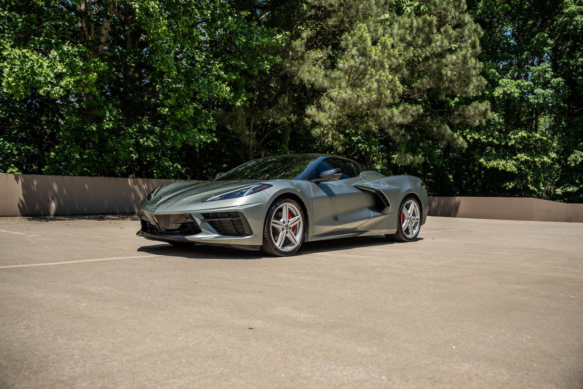 Silver sports car parked in a paved lot, with trees in the background.