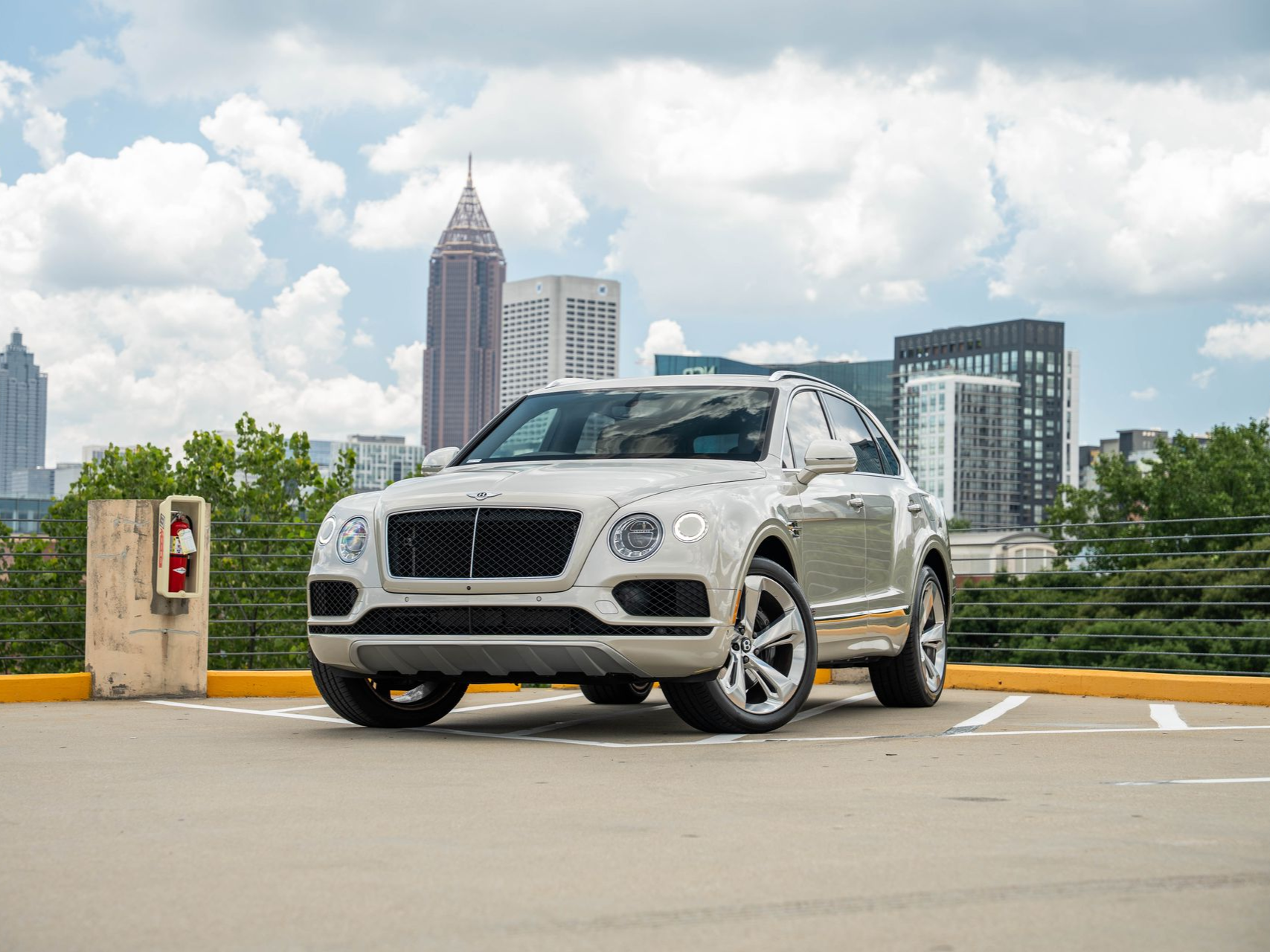 Silver Bentley SUV parked on a rooftop with Atlanta skyline in the background.