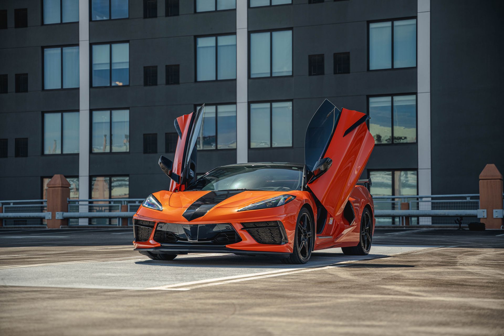 Orange sports car with doors open, parked on a rooftop. Black accents.