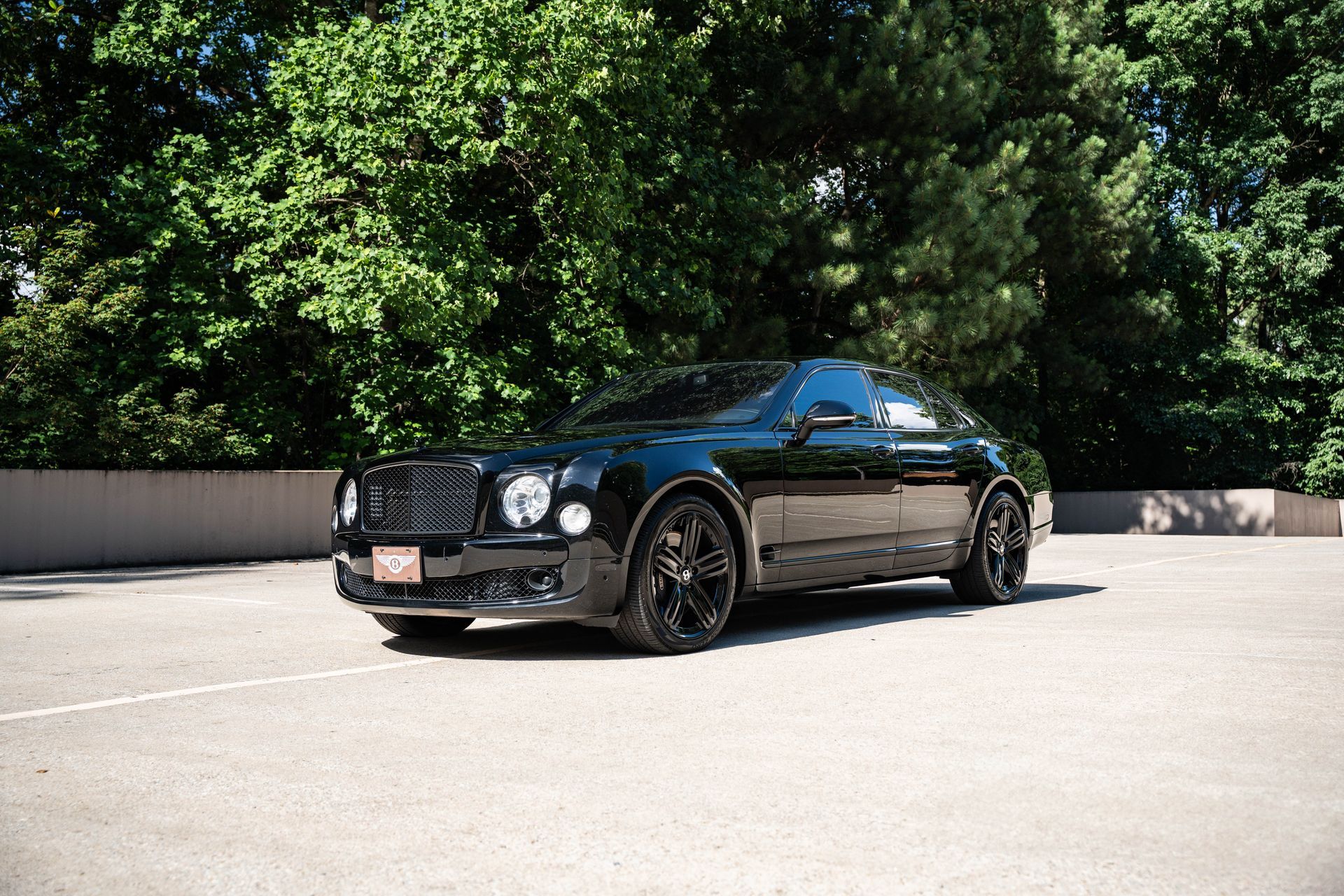 Black Bentley sedan parked in a parking lot, with trees in the background.