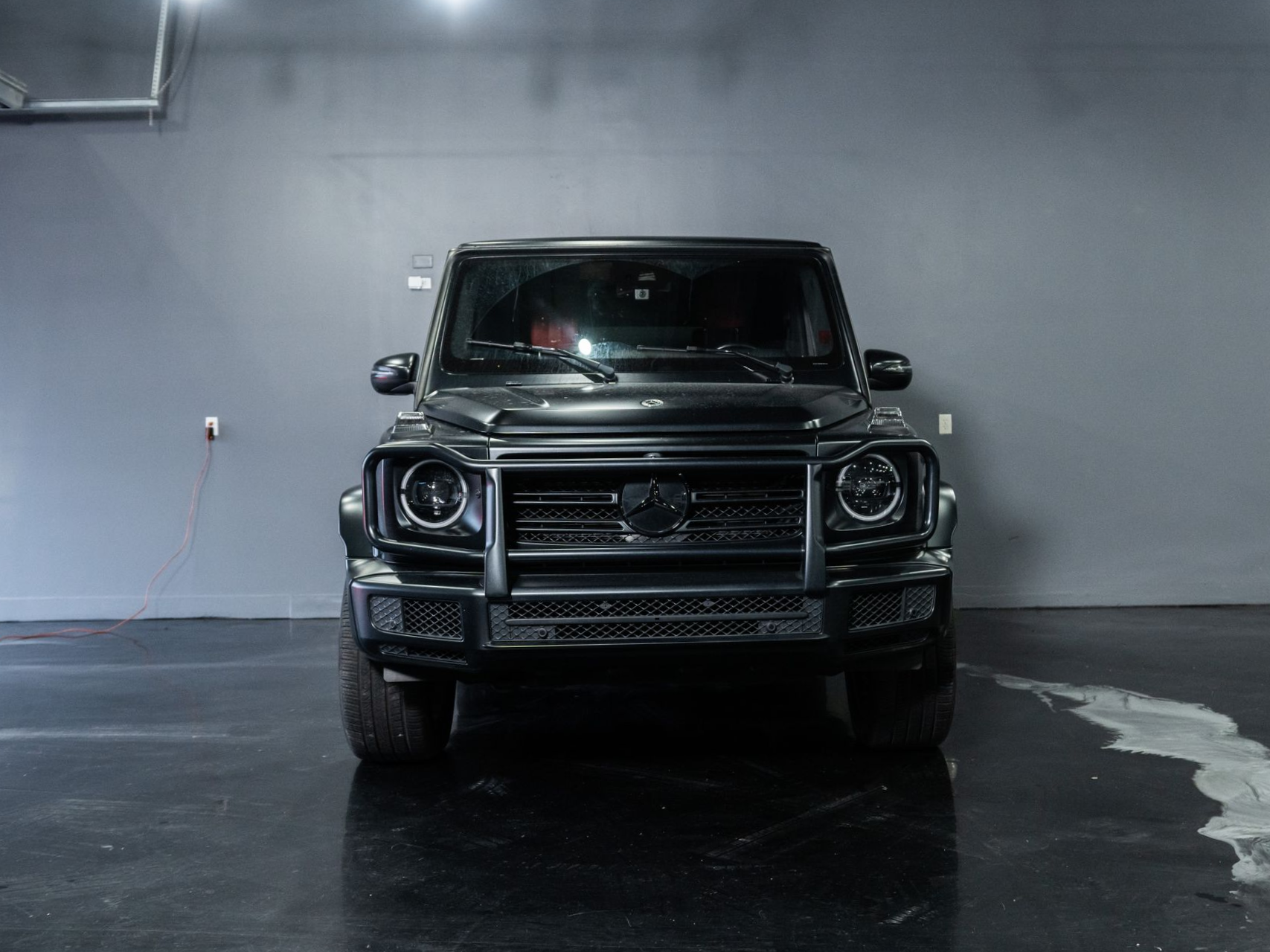 Black Mercedes-Benz G-Class SUV parked indoors on a wet concrete floor against a gray wall