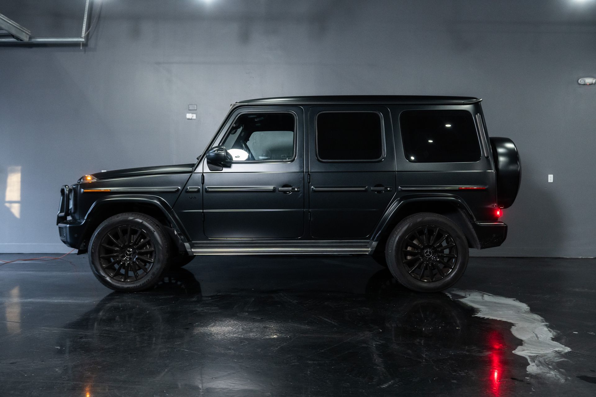 Black SUV parked in a dim garage, side view with wet floor reflections