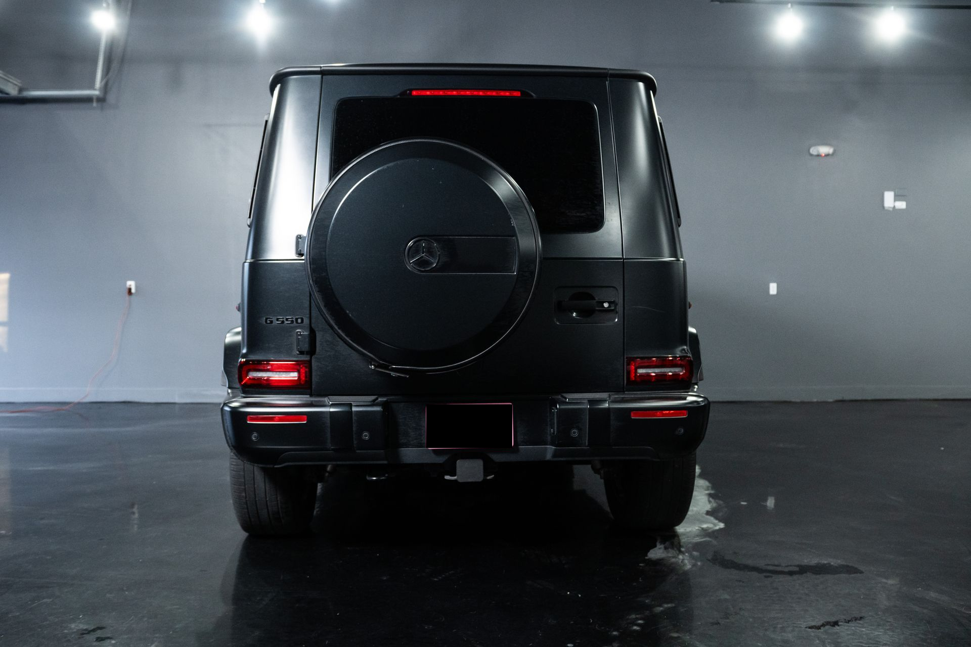 Rear view of a black Mercedes G-Class SUV in a dim garage, with taillights on.