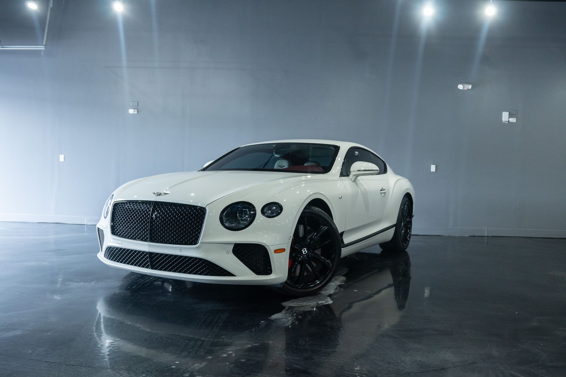 White Bentley coupe parked on a glossy surface under bright lights.