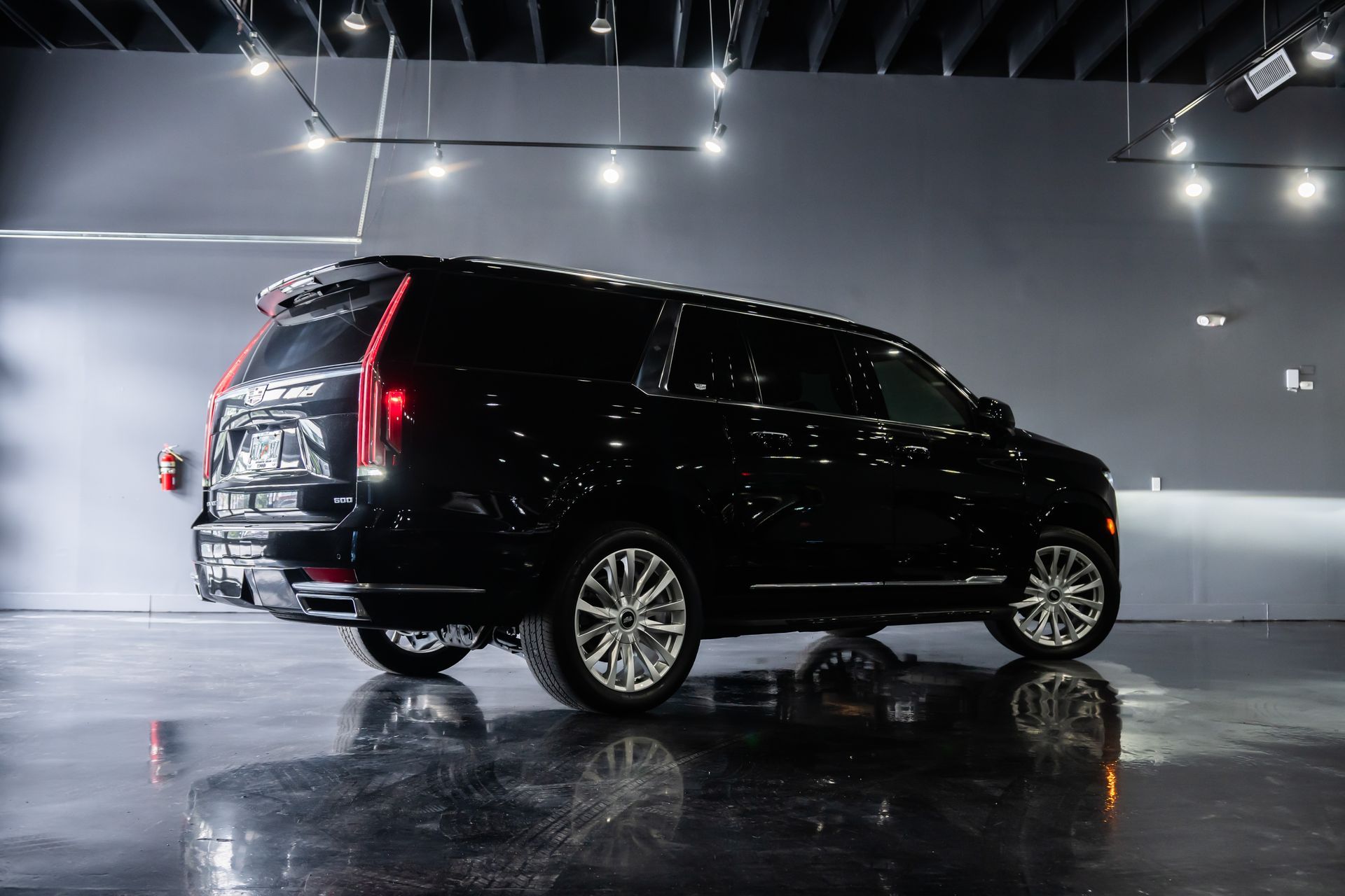 Black van in a glossy showroom, seen from the rear-left under bright overhead lights.