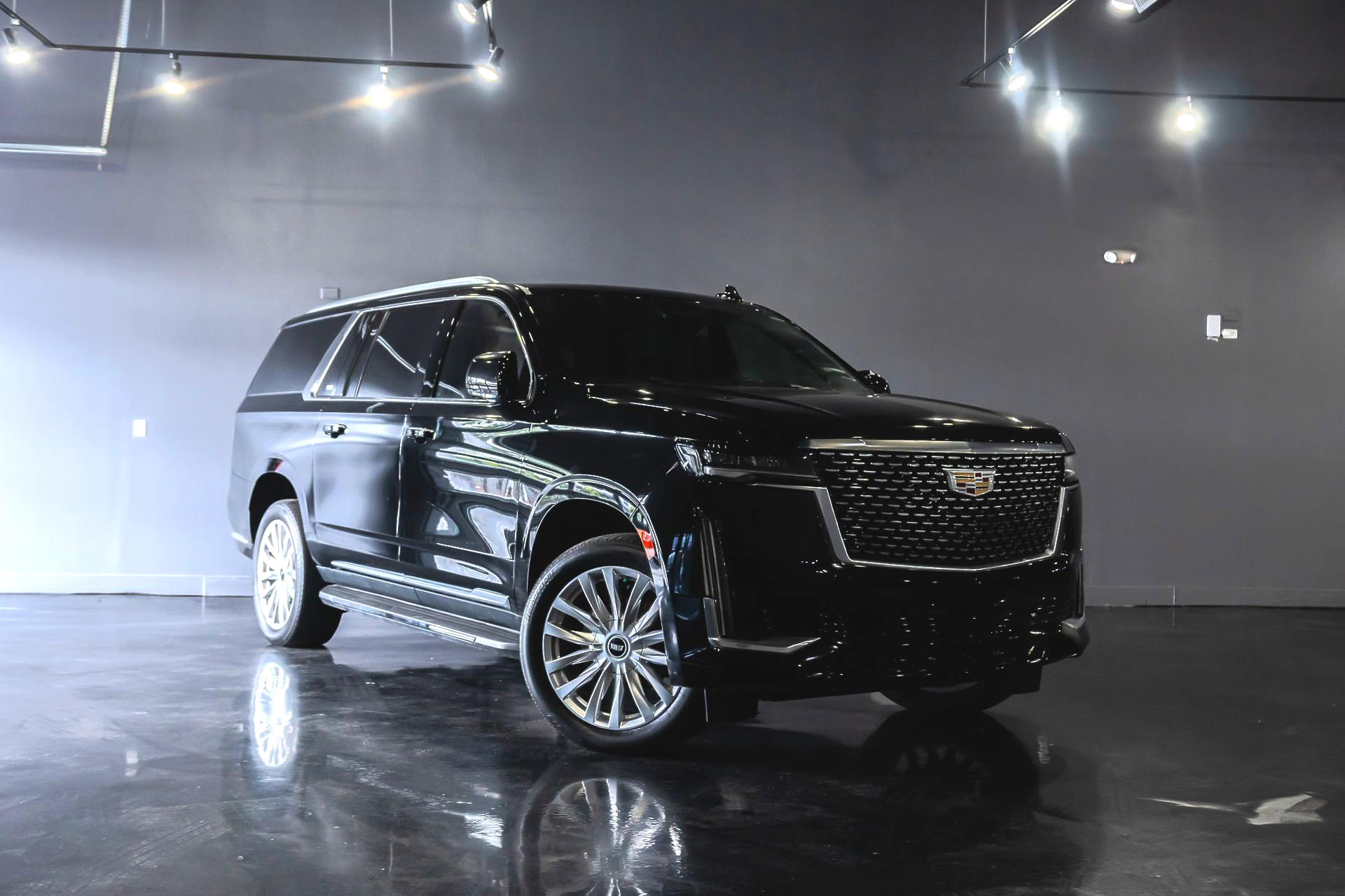 Black SUV in a glossy showroom, lit by overhead string lights, reflecting on the polished floor.
