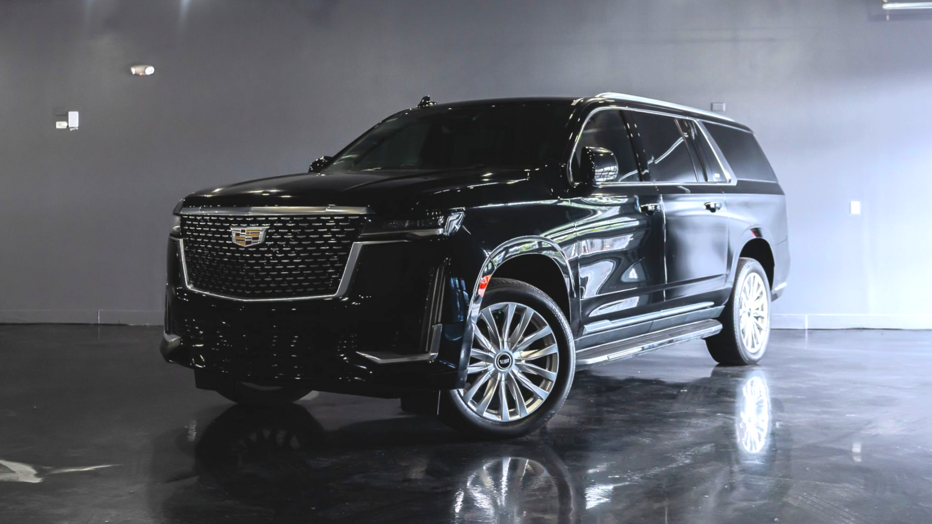 Black Cadillac SUV parked in urban area, city skyline in background.