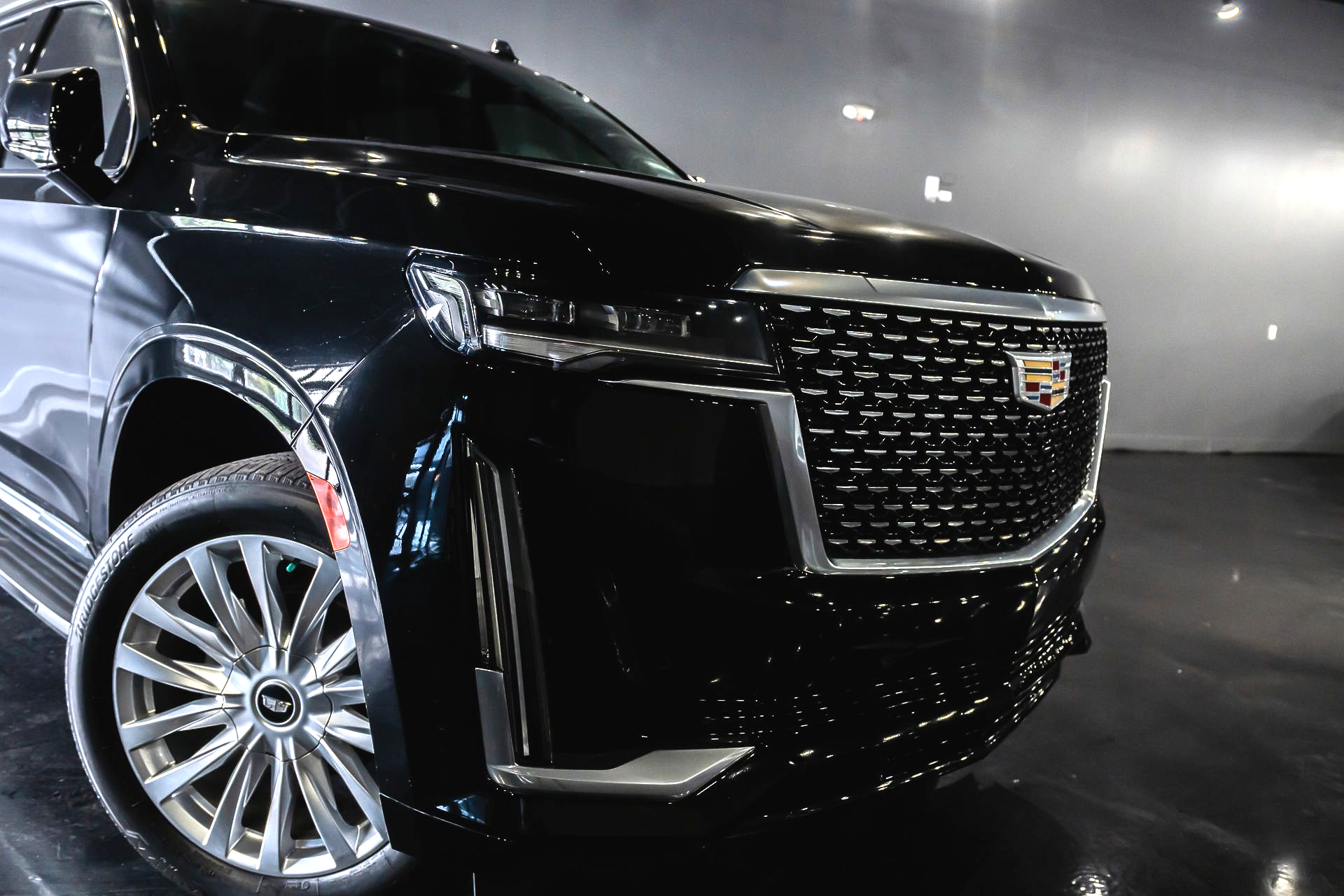Black Cadillac SUV displayed indoors, front view with chrome grille and silver wheel accents
