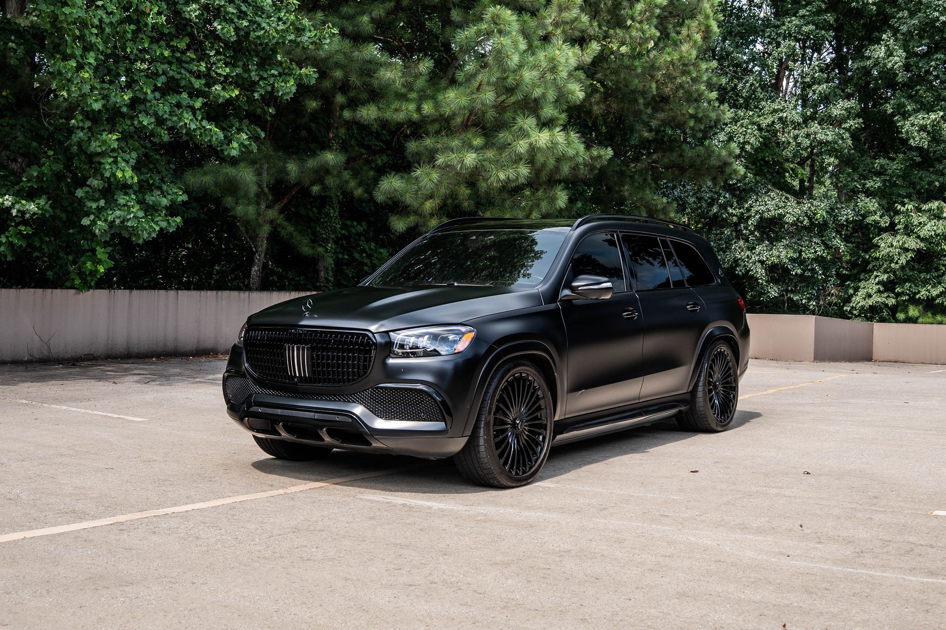 Black SUV parked in a lot, with tinted windows and dark rims, in front of green trees.
