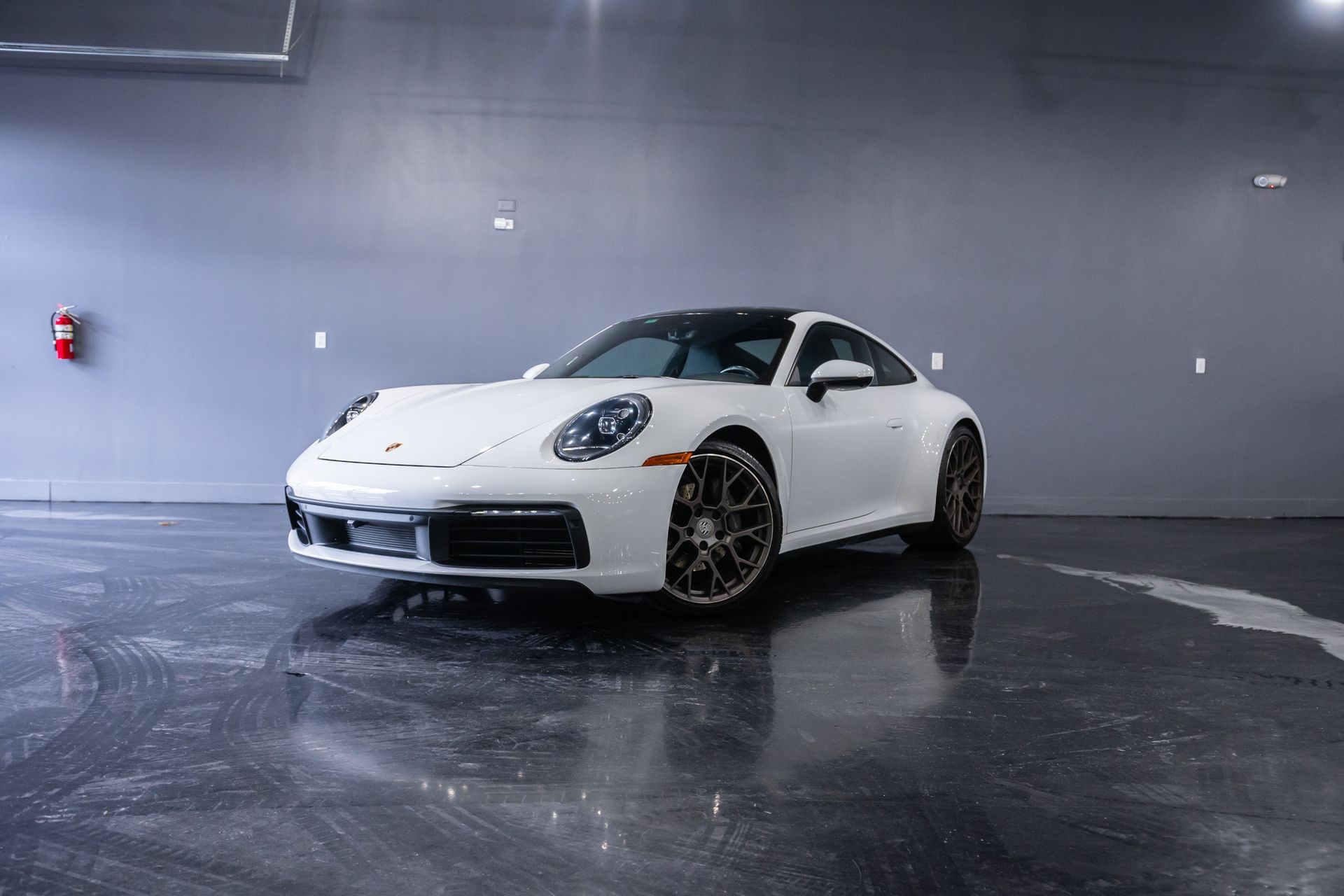 White Porsche 911 coupe parked on a glossy floor in a garage with reflective surfaces.