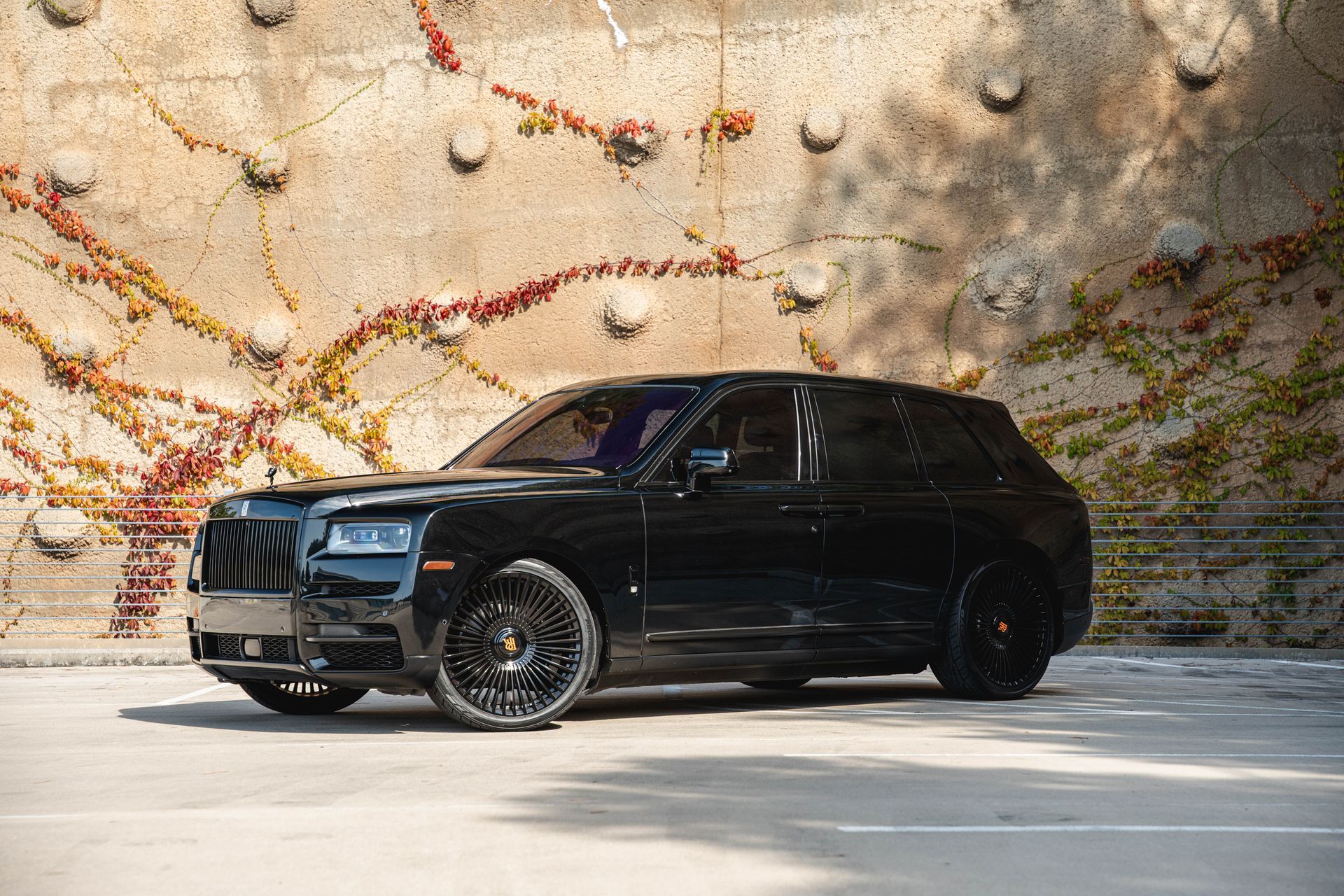 Black Rolls-Royce Cullinan SUV parked in front of a textured wall with climbing plants.