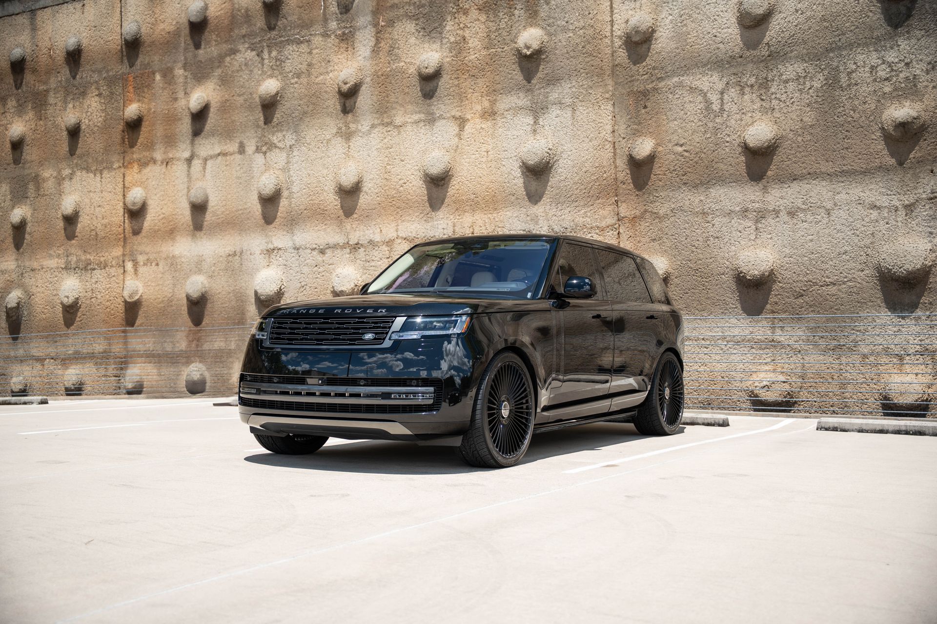Black Range Rover SUV parked in front of a textured concrete wall on a sunny day.