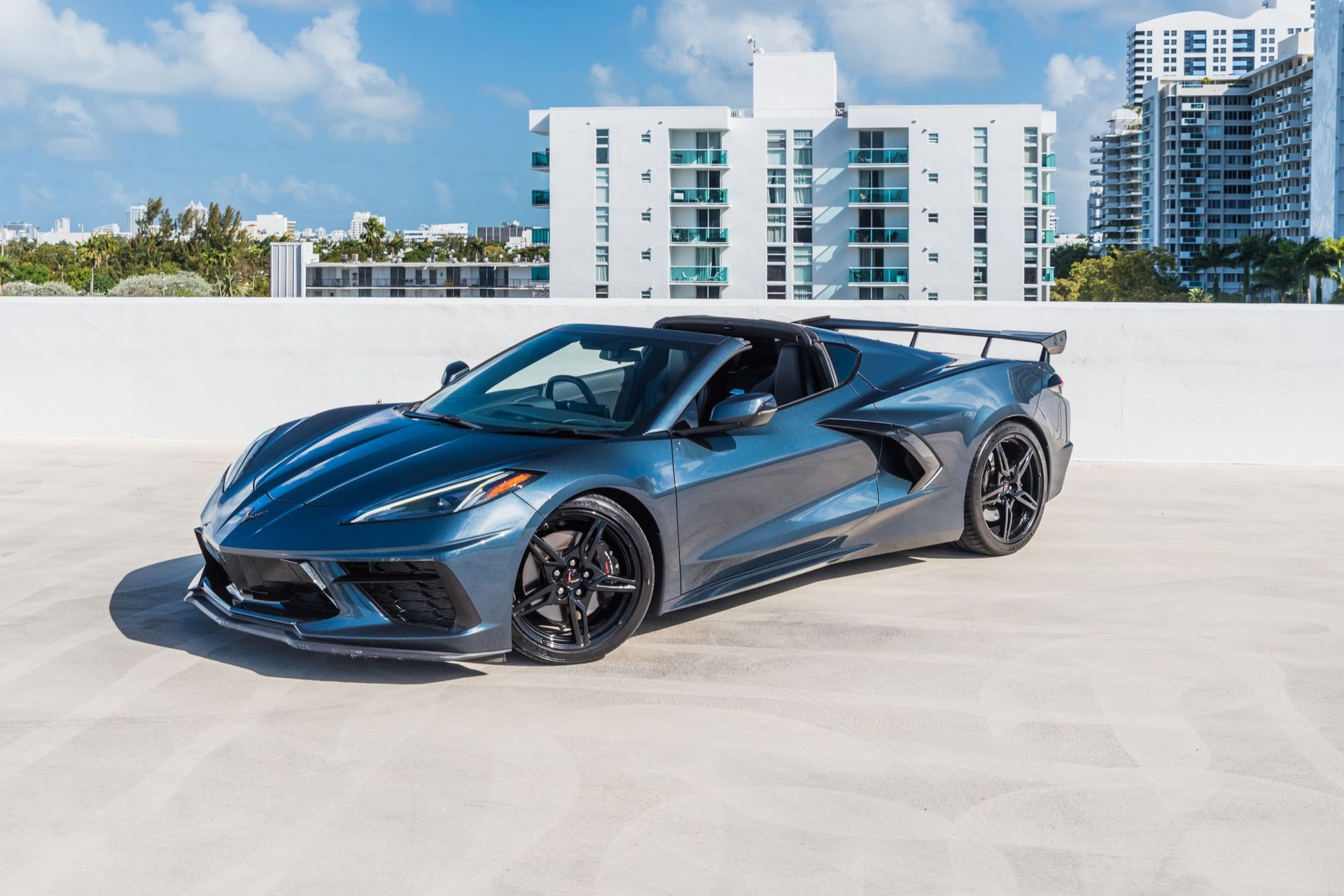 Blue convertible sports car parked on rooftop with cityscape background.