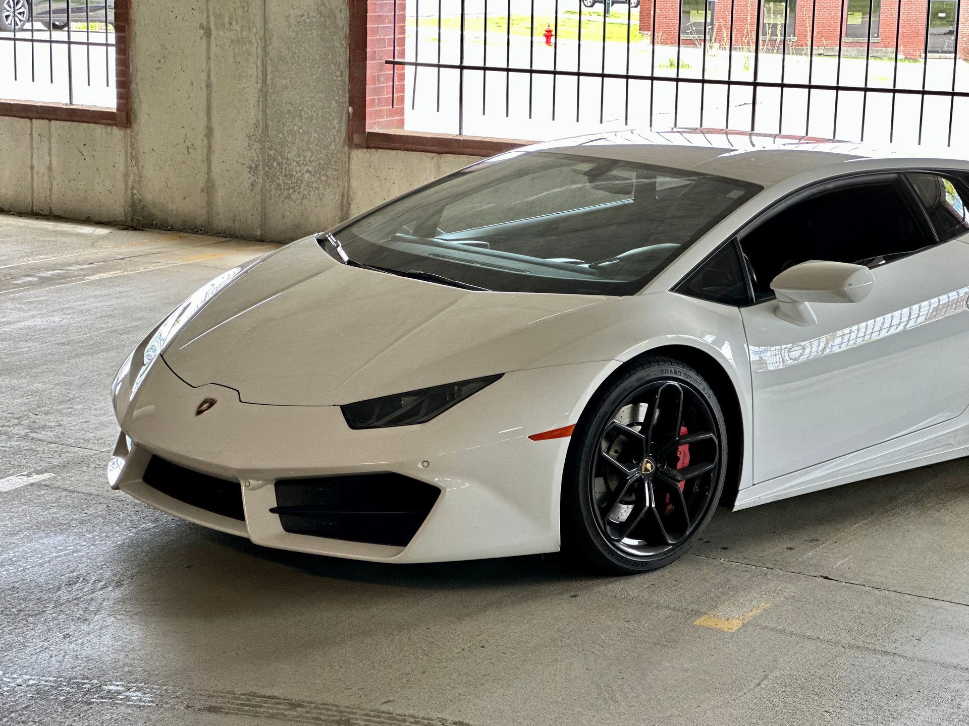 White sports car in a concrete garage, front-left view, with dark tinted windows and black wheels