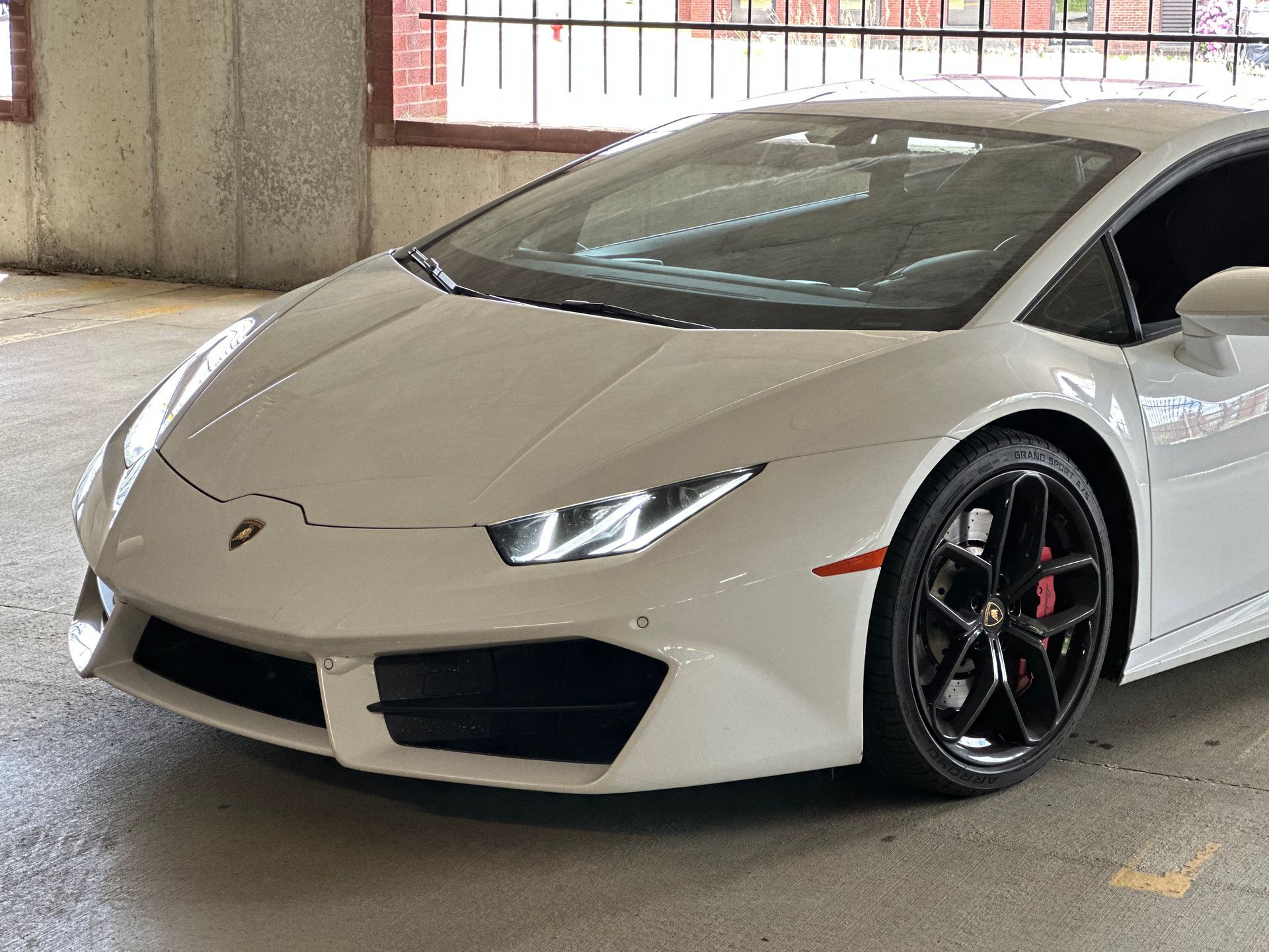 White Lamborghini parked indoors, front-left view, under a concrete structure.