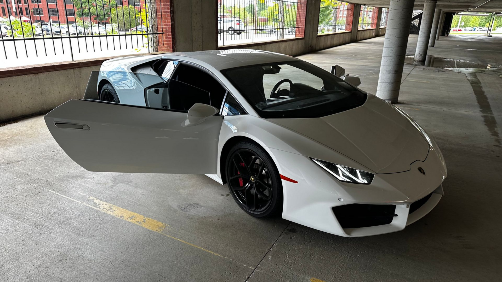 White sports car with one door open, parked in a concrete garage