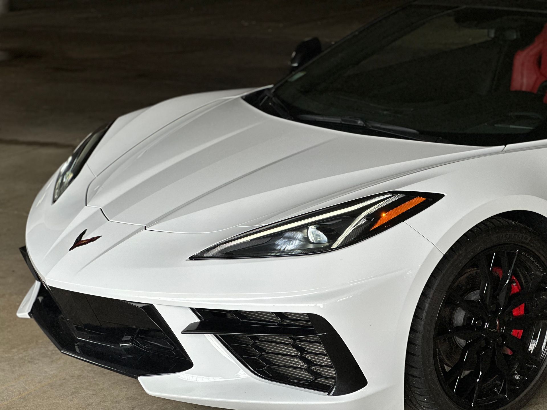 White sports car with black wheels and red brake calipers, shown front-left on a dark background
