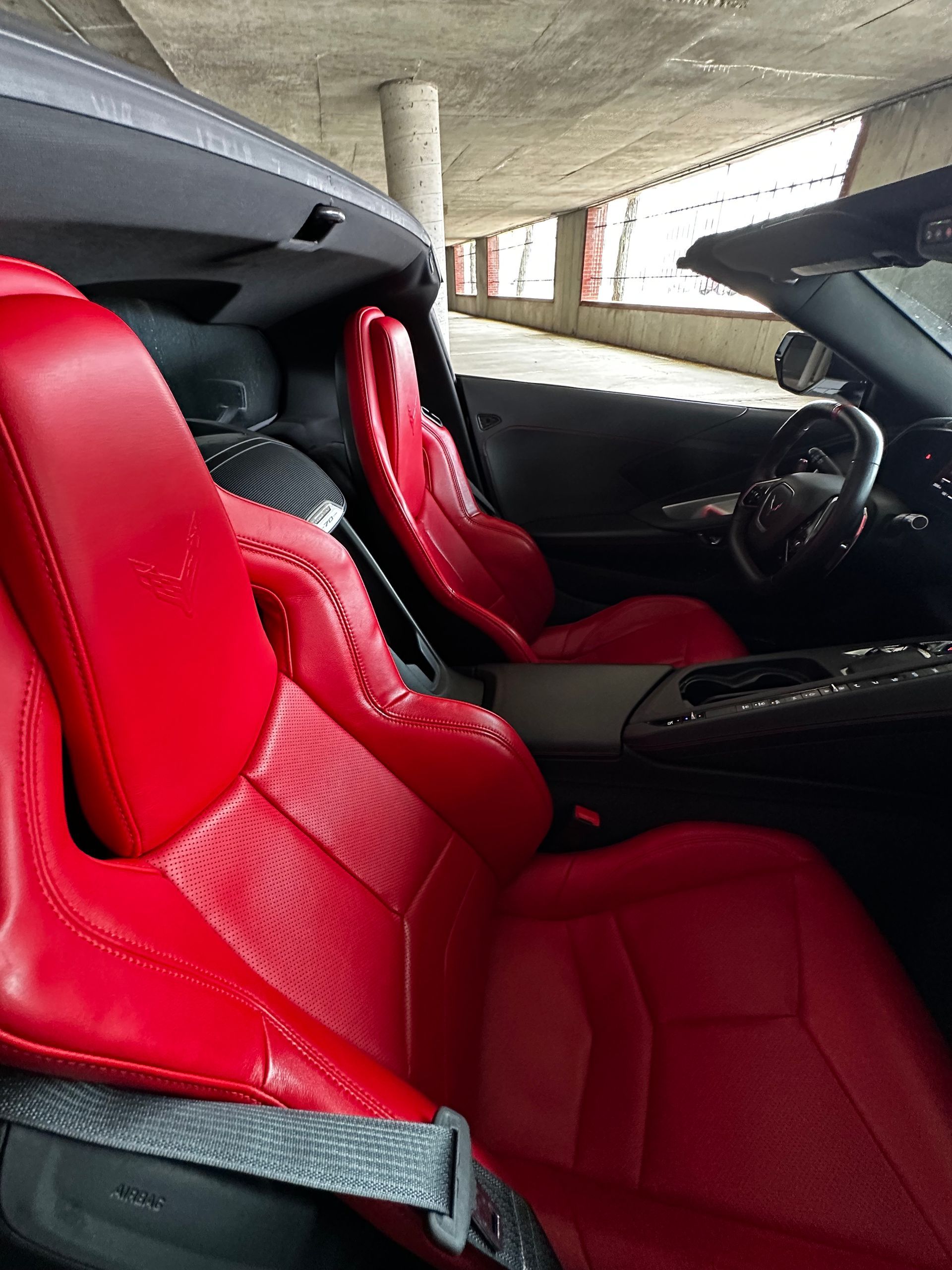 Red leather sports car interior with two bucket seats and a black dashboard in a parking garage