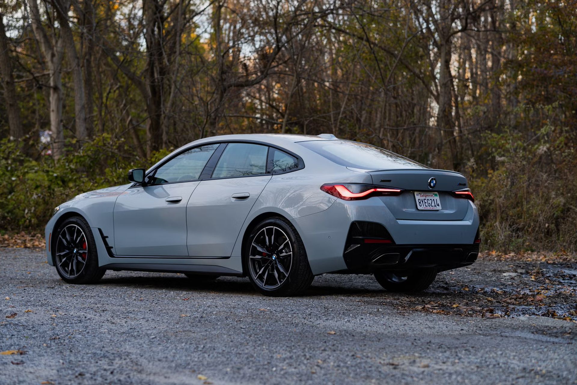 Silver sedan parked on a gravel road beside a wooded area in autumn.