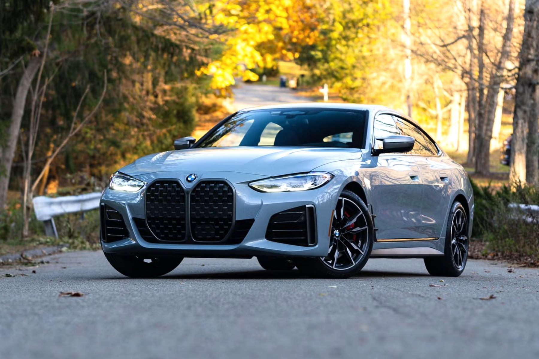 Silver BMW sedan parked on a wooded road with autumn trees in the background