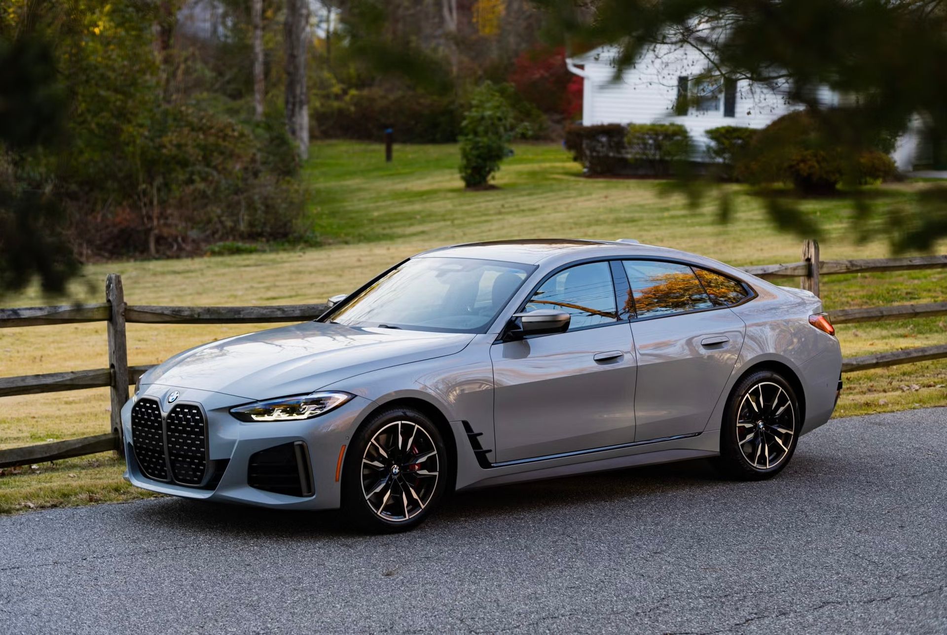 Silver BMW sedan parked on a road beside a wooden fence, with trees and houses in the background