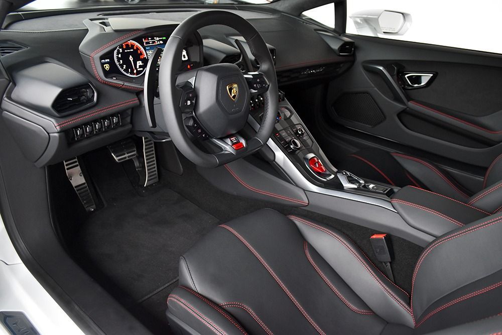 Luxury sports car interior with black leather, red stitching, and a steering wheel featuring a Lamborghini logo