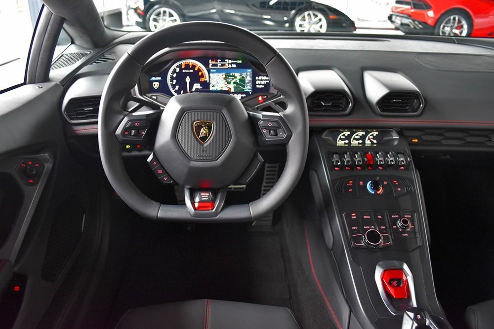 Lamborghini sports car interior, showing the steering wheel, digital dashboard, and center console with red accents
