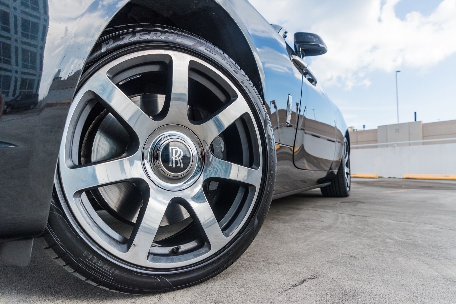 Close-up of a shiny black Rolls-Royce wheel, silver and chrome, parked on a rooftop.