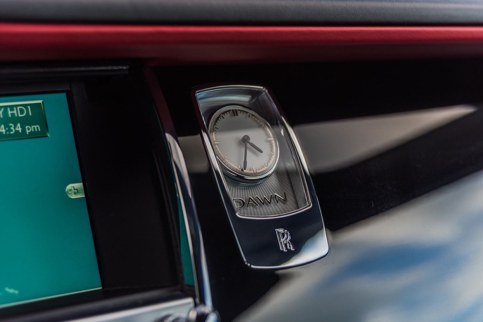 Chrome clock in a Rolls-Royce dashboard, featuring the Rolls-Royce logo and a teal touchscreen display.